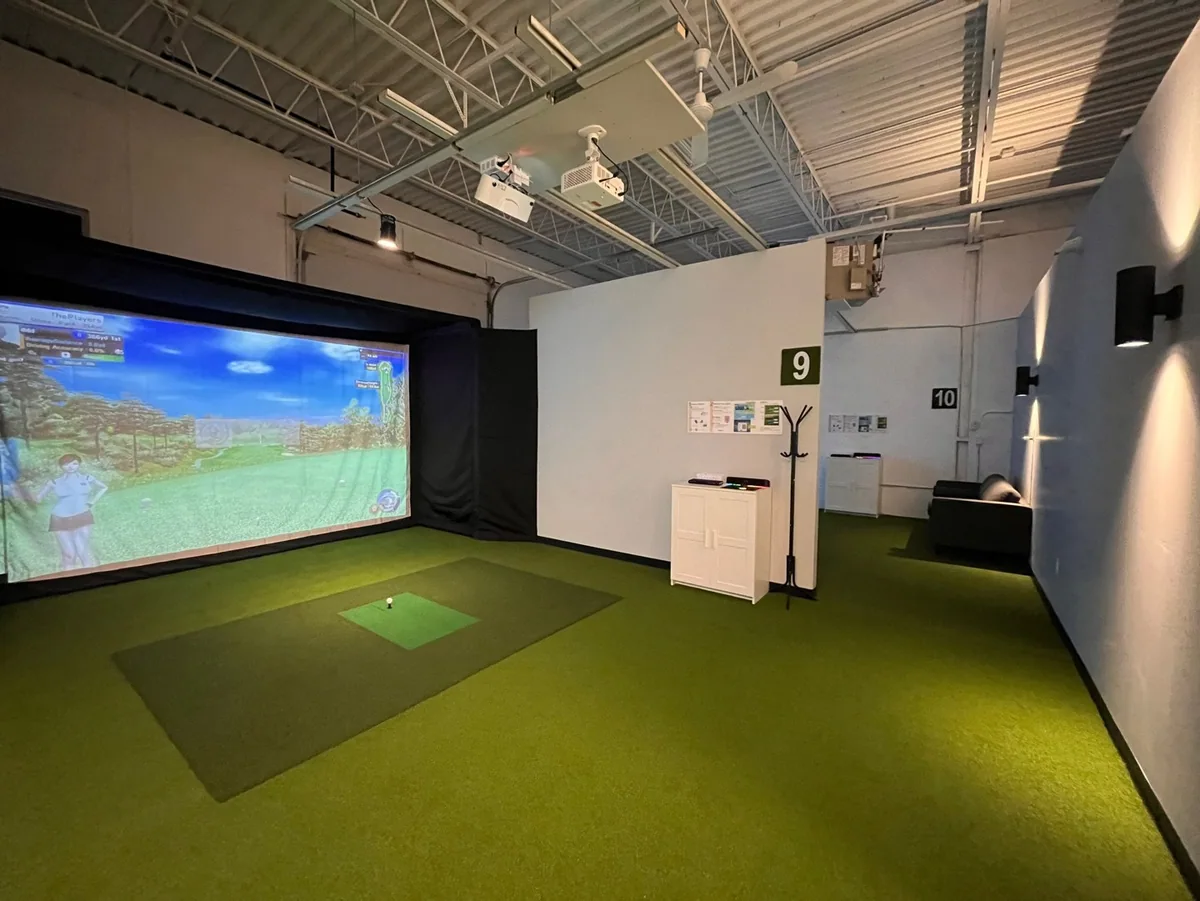 A bright simulator installation with a screen, hitting mat and divided bays