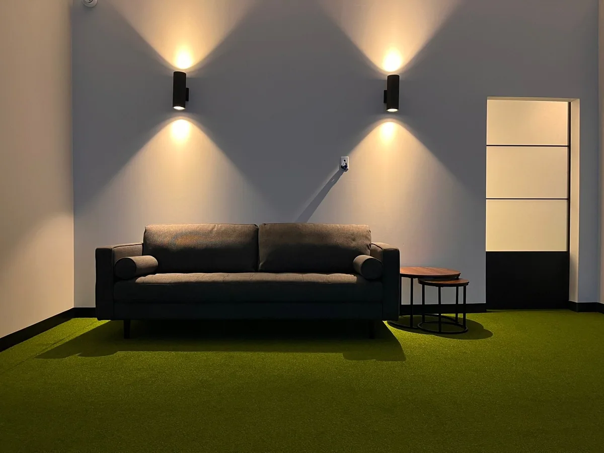 A seating area with a sofa and wall lighting next to a simulator space
