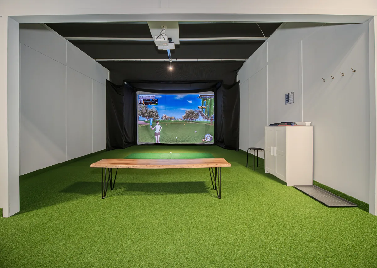 Front view of a spacious simulator bay with a hitting mat and a wooden bench
