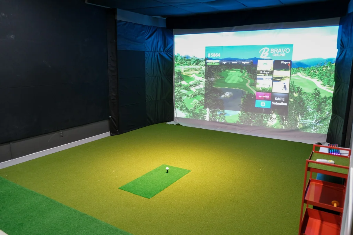 A dedicated golf simulator room with a screen, hitting mat and control cabinet