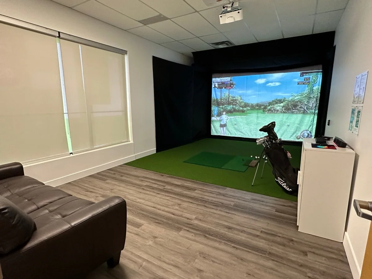 An enclosed simulator room with a sofa, golf bag and equipment cabinet