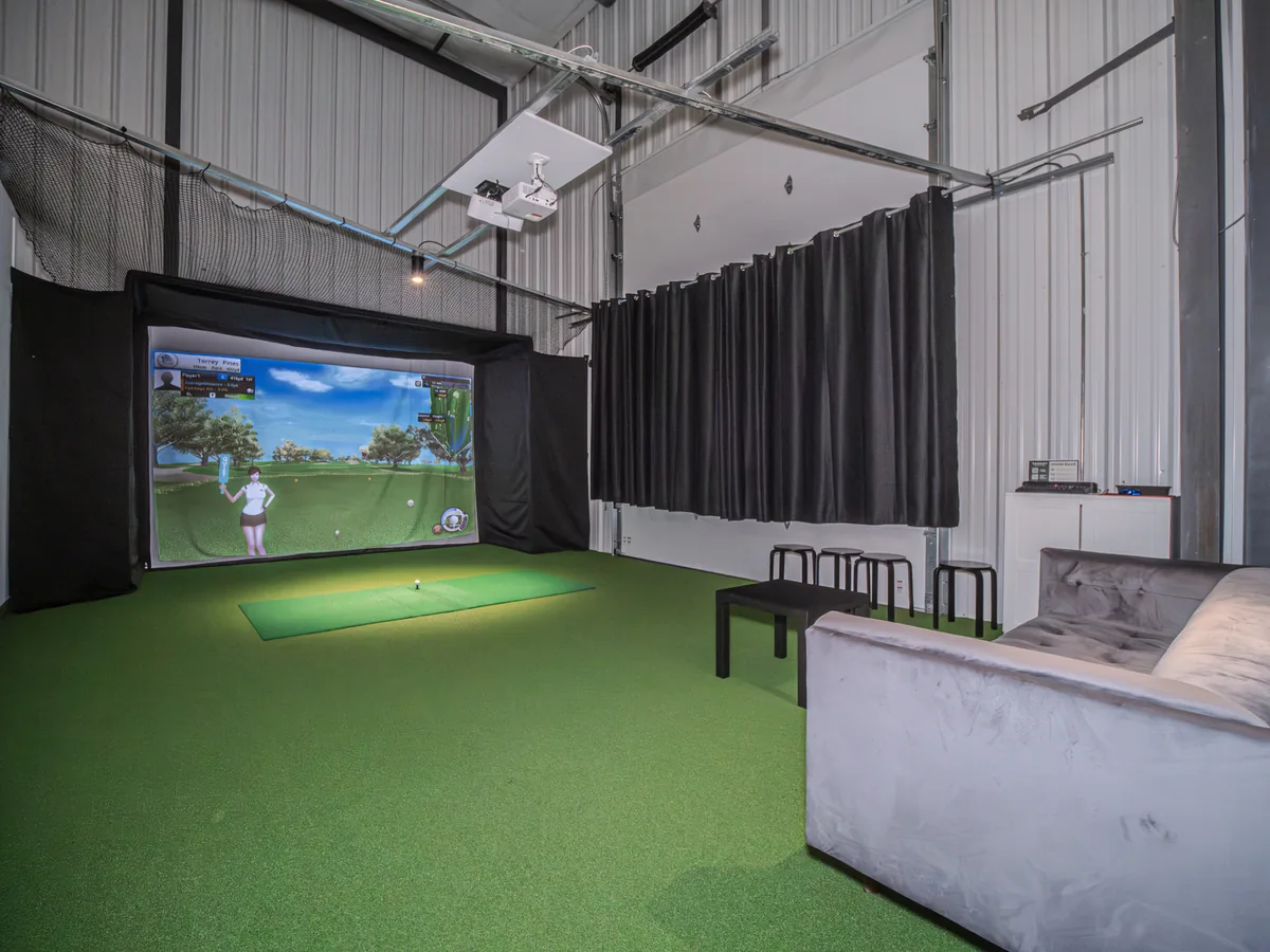 A simulator room with lounge seating, an impact screen and overhead equipment