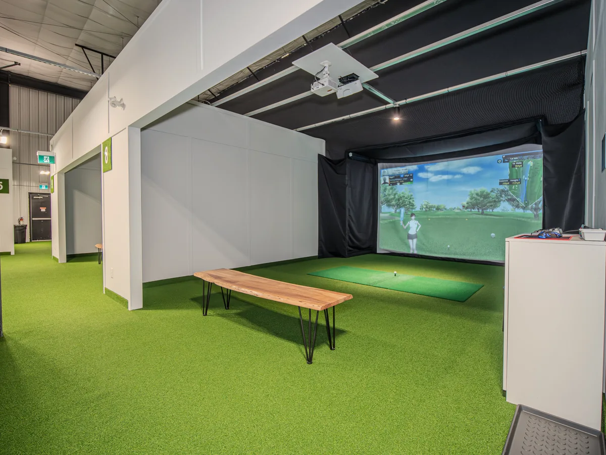 A bright simulator bay with an impact screen, hitting mat and overhead equipment